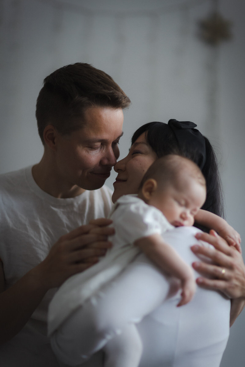 Loving parents cradling their sleeping baby, all dressed in white for a calming and comfortable photo shoot at home