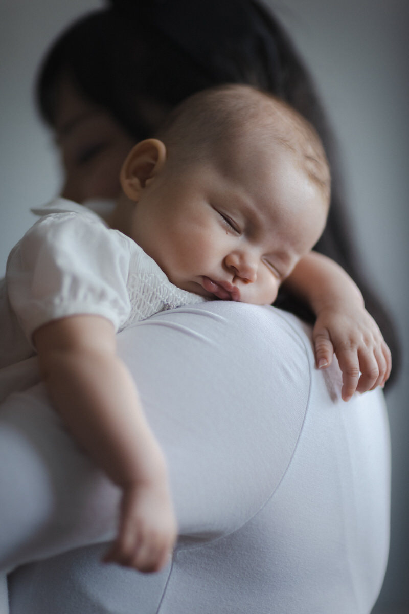 Portrait of a happy family, with parents dressed in white and holding their newborn baby during a photo session at home.