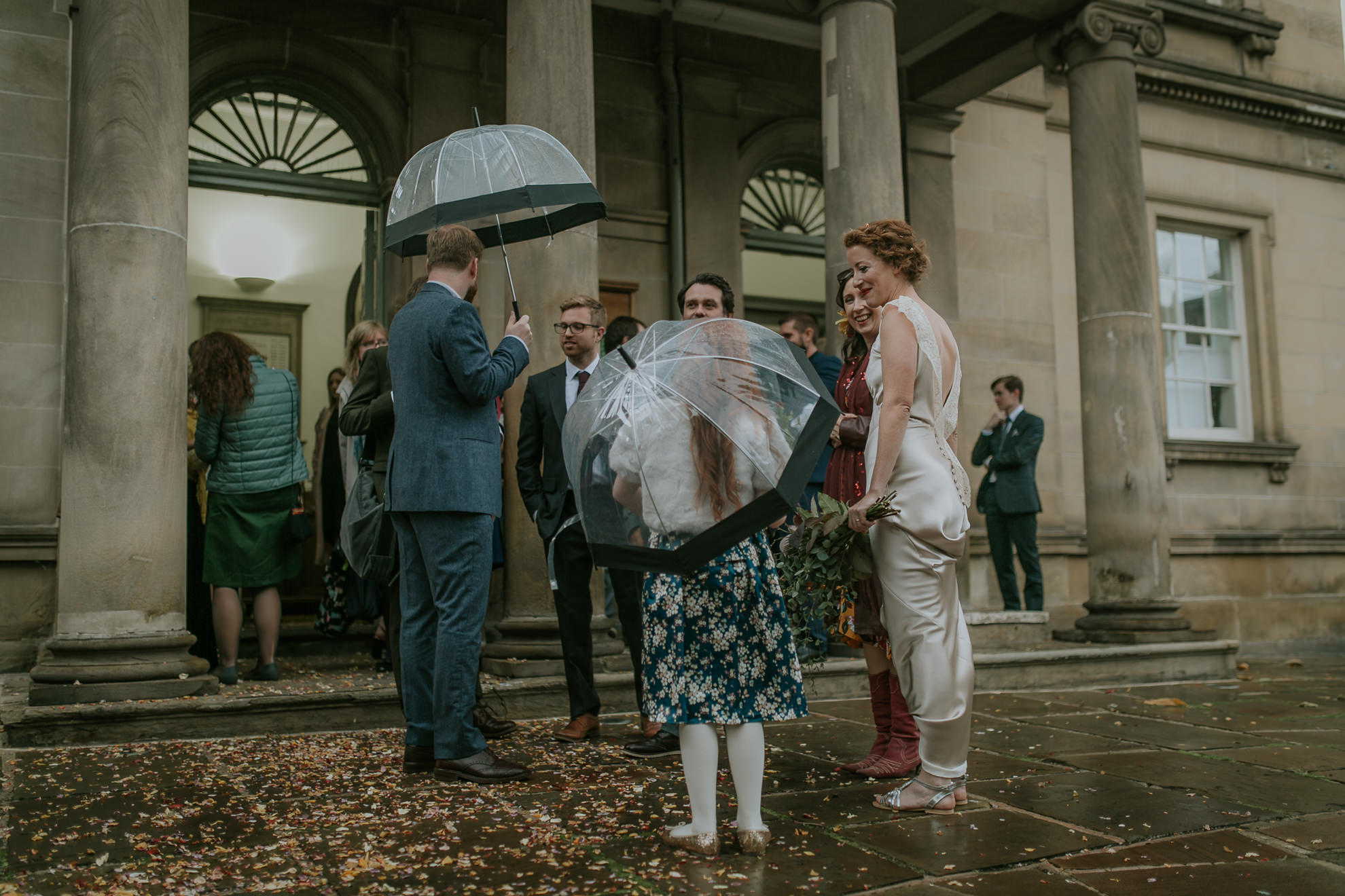 Bride and groom talking to a young girl outside on a rainy day
