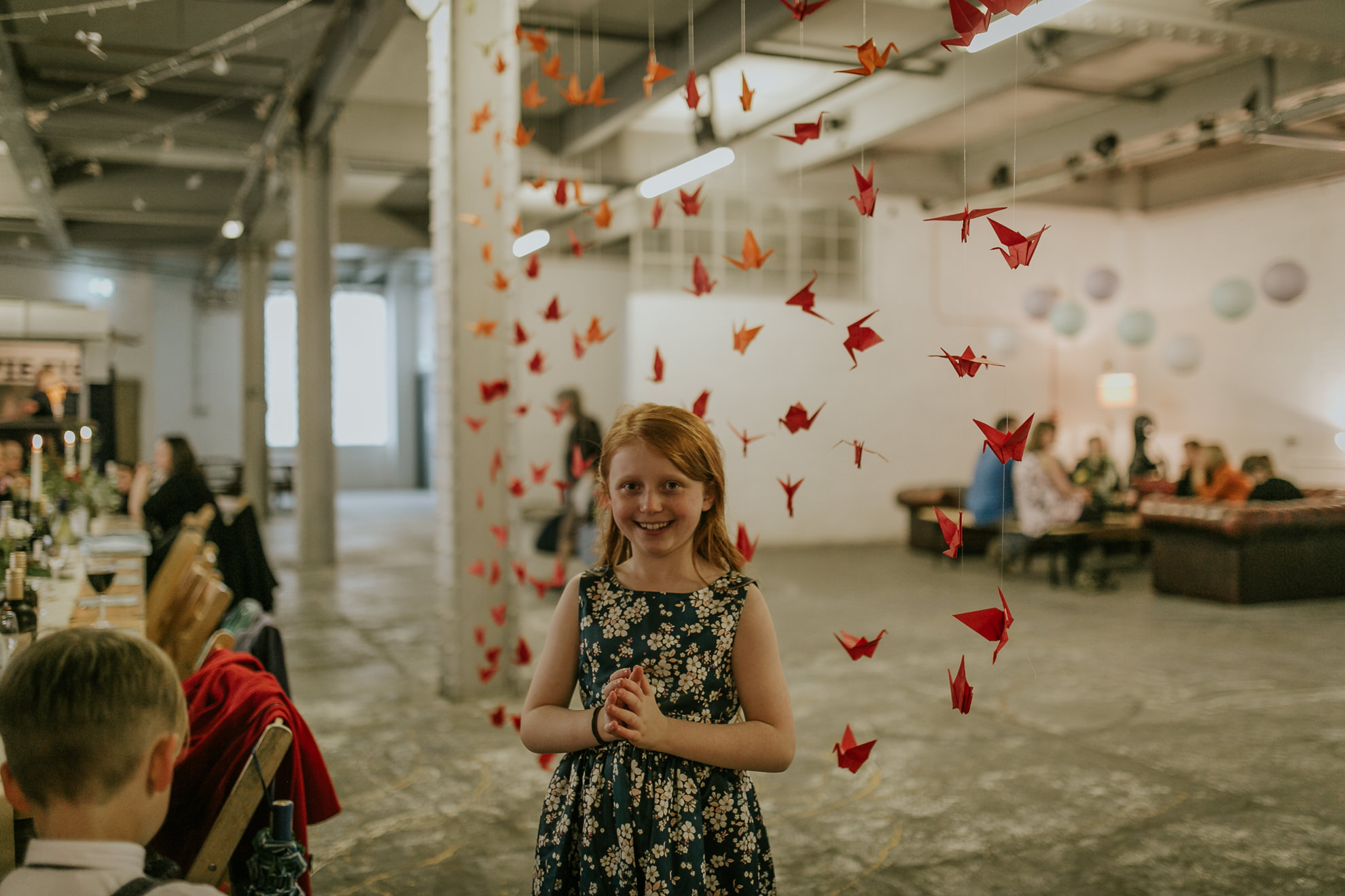 Girl with Red hair in Trafalgar Warehouse smiling at a net of red origami birds