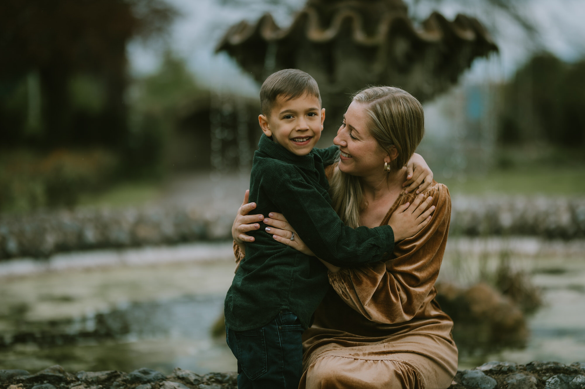 Mother and young son smiling at each other sitting near a water fountain